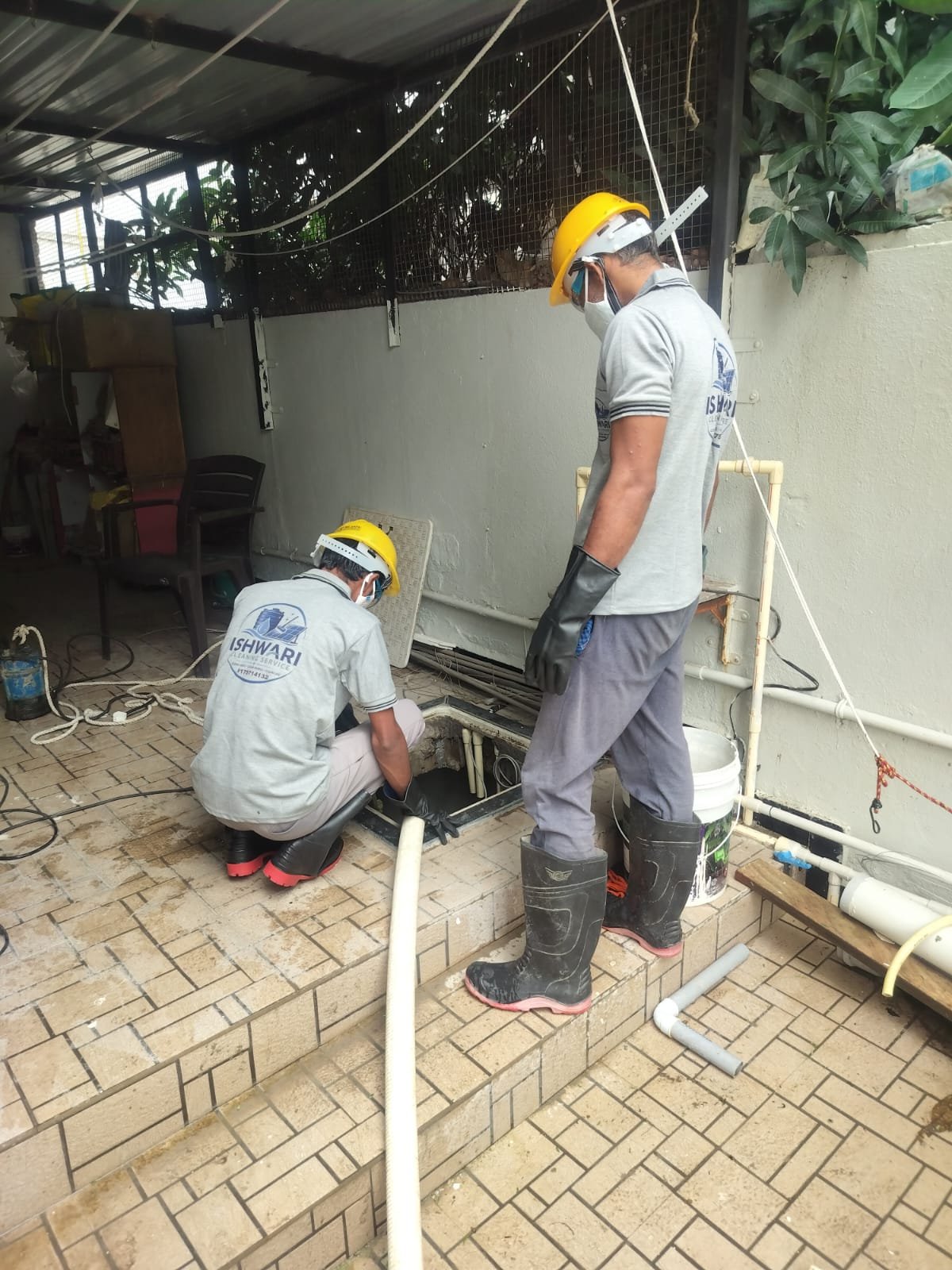 Two technicians carefully working beside a water tank hatch